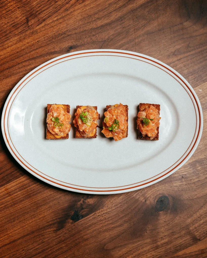 Four raw fish appetizers on toast, topped with green onions.
