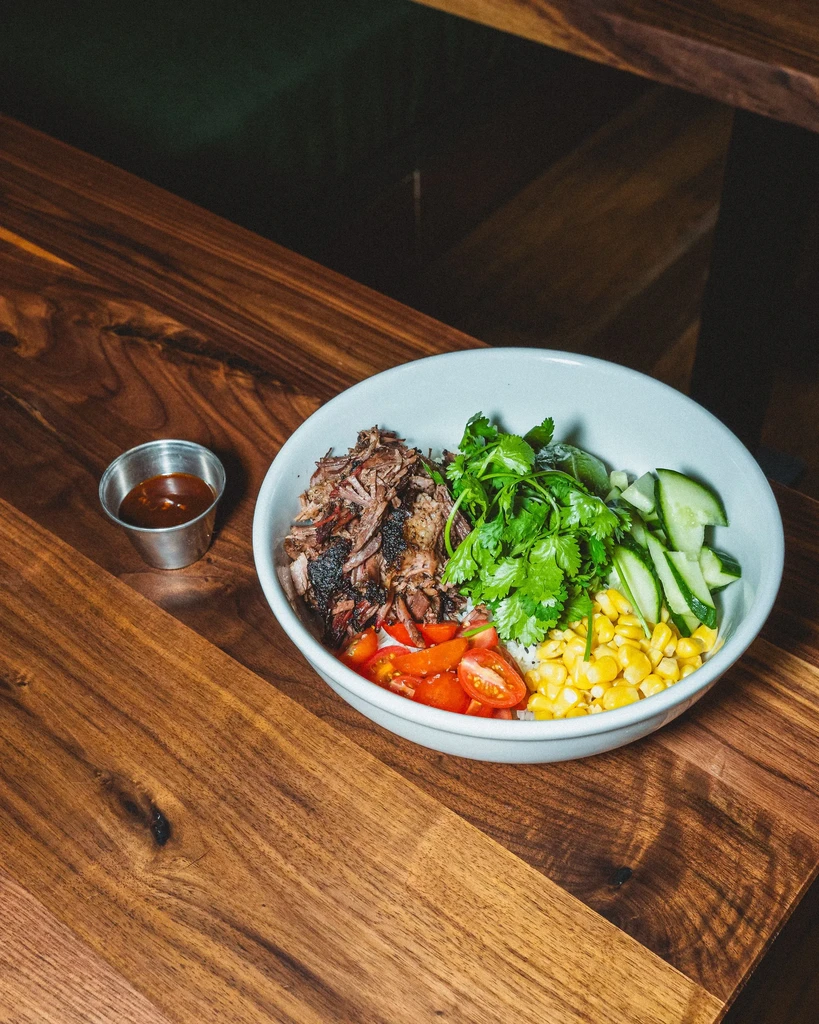 Bowl with shredded meat, cilantro, cucumber, corn, tomatoes, side sauce.