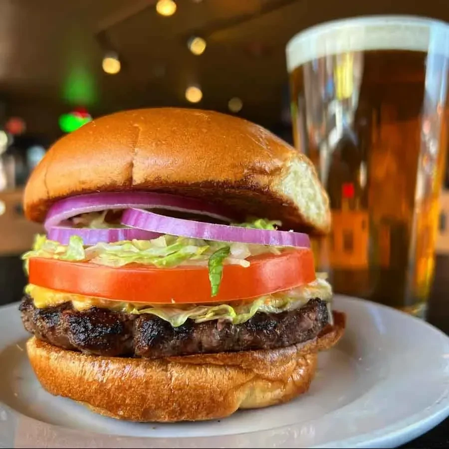 Gourmet hamburger with melted cheese, fresh vegetables, and a glass of beer.