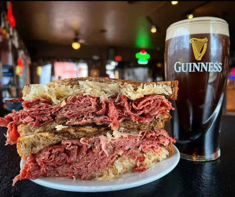Stacked Reuben sandwich and Guinness pint on plate in pub.