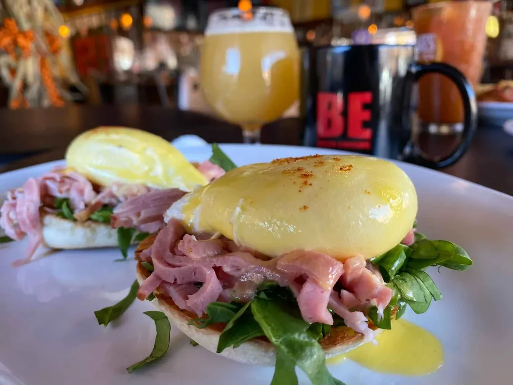 Warm close-up of two ham Eggs Benedict plates at a restaurant.