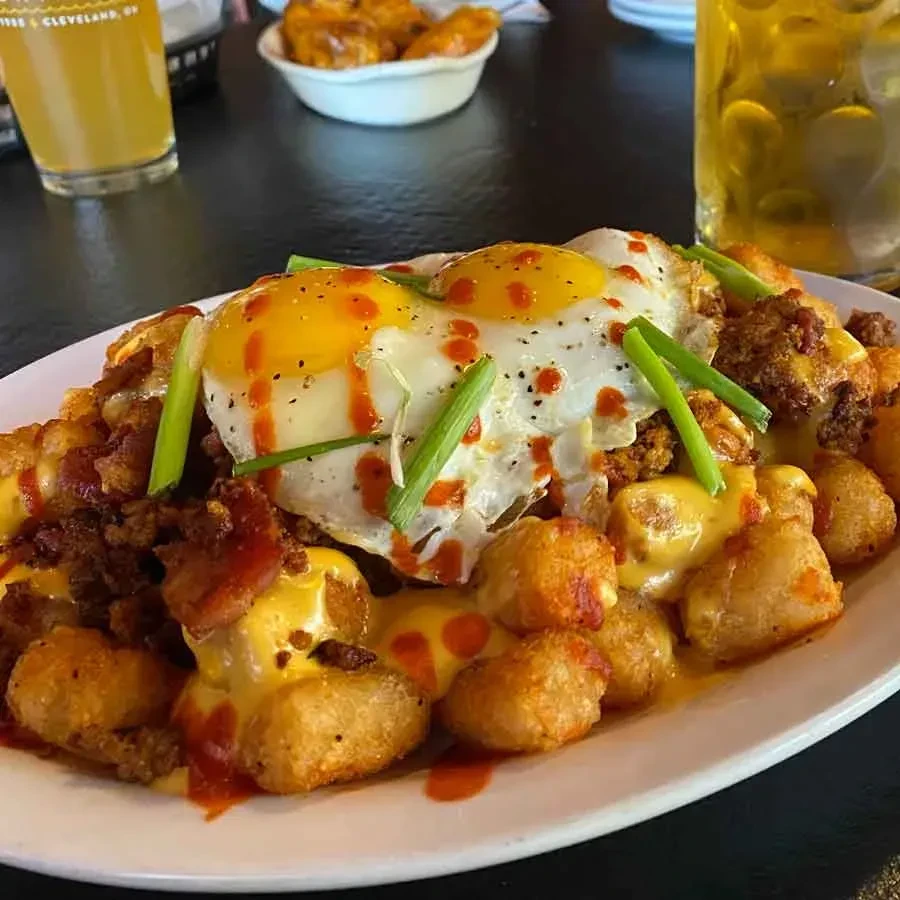 Tater tots with cheese, meat, fried eggs, hot sauce, and green onions.