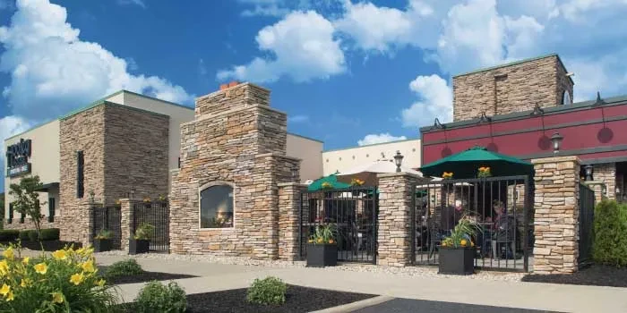Stone restaurant exterior, outdoor patio with diners under green umbrellas.