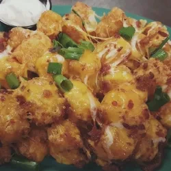 Loaded tater tots with melted cheese, bacon, green onions, and side sauce.