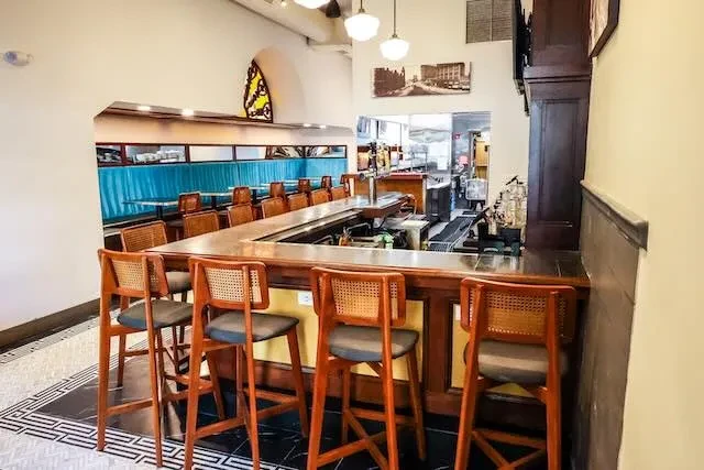 Empty classic bar interior with L-shaped counter and teal booths.
