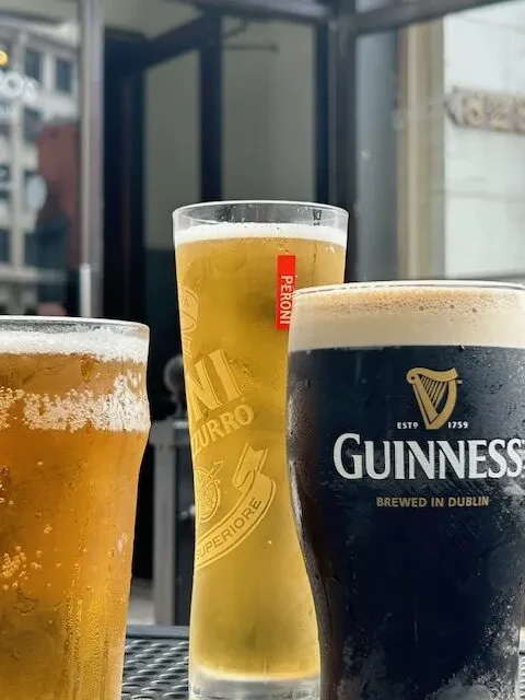 Three cold beers: light, Peroni lager, and Guinness stout on patio.