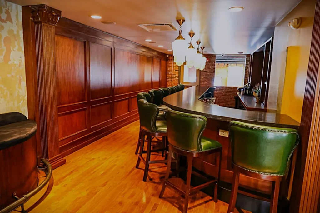 Sophisticated bar interior with dark counter, green stools, wood paneling, warm light.