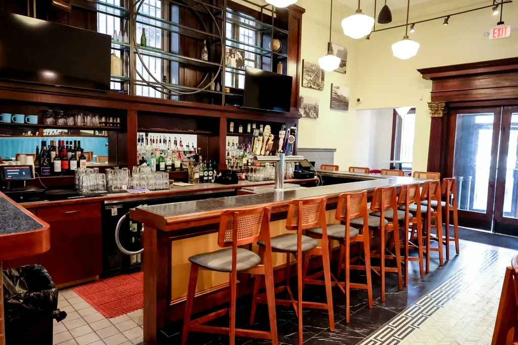 Empty, clean bar with a curved counter, liquor bottles, and stools.