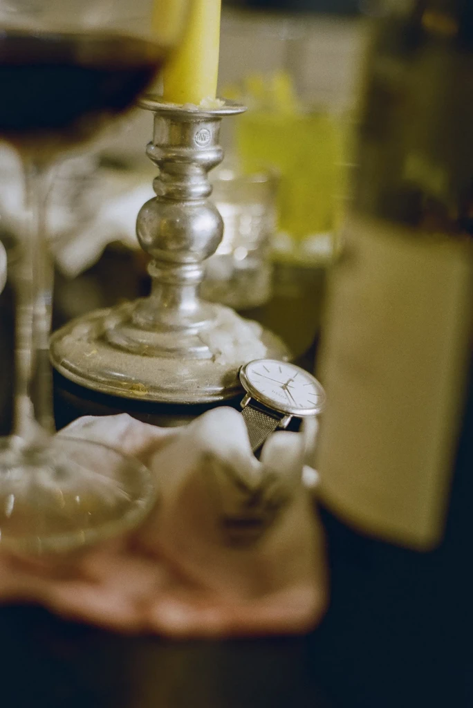 Close-up of burning candle in antique candlestick, watch, and red wine.