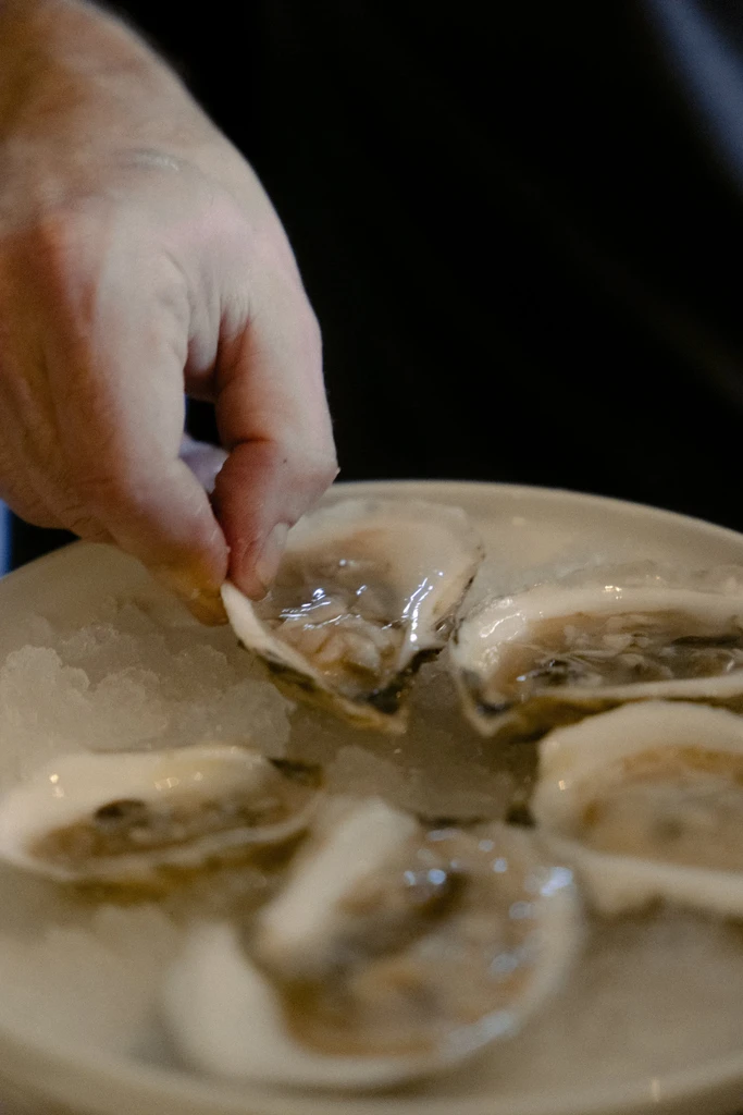 Fresh raw oysters on crushed ice, a hand picking one up.