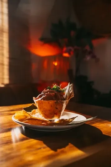 Reddish-brown dip garnished with herbs and tortilla chips on a wooden table.