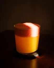Layered orange drink with frothy foam, dramatically lit.