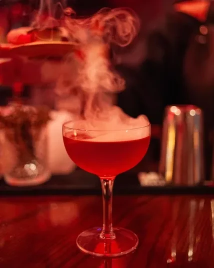 Vibrant red cocktail in coupe glass, dense white smoke emanating.