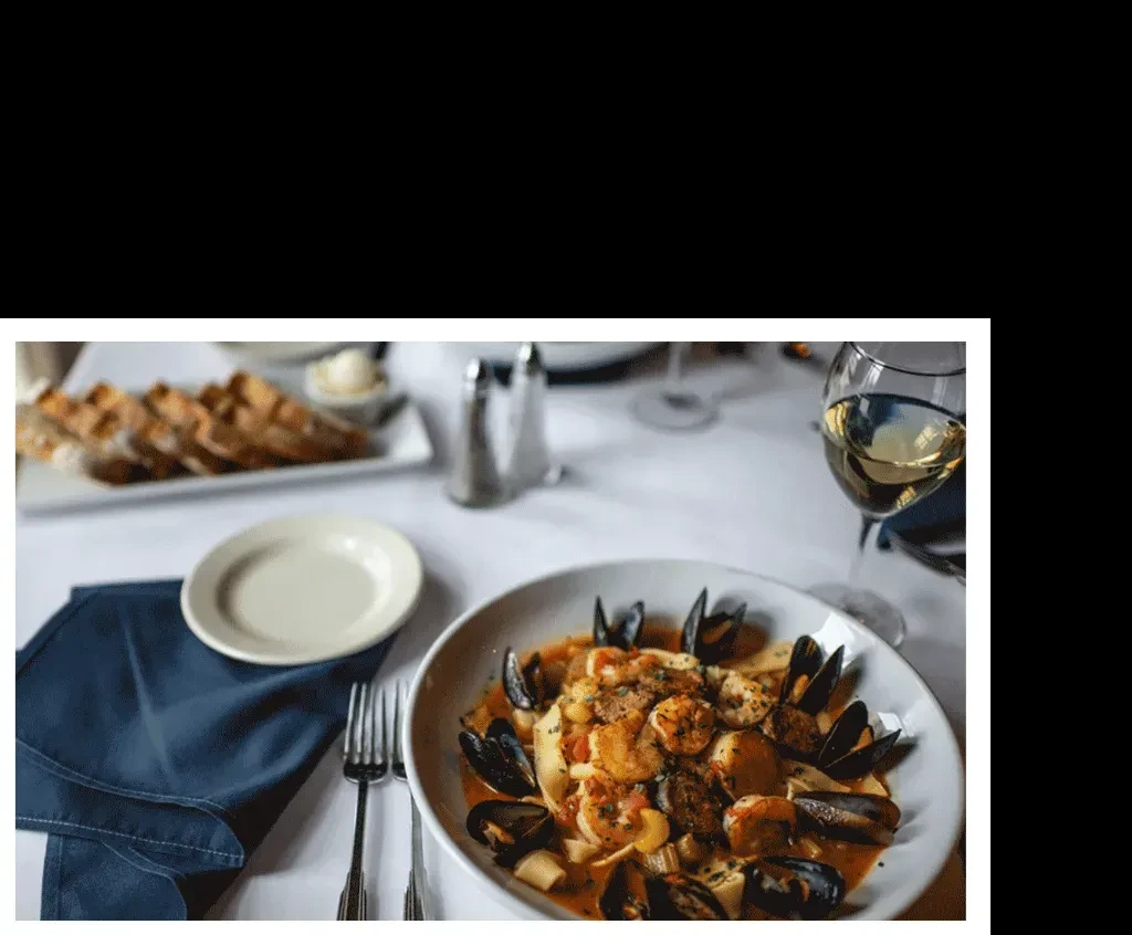 Seafood pasta with mussels, shrimp, wine, and bread on table.