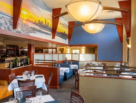 Restaurant interior: blue booths, set tables, cityscape mural, visible bar.