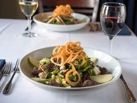 Two gourmet salads with meat, cheese, apples, onion rings and wine.