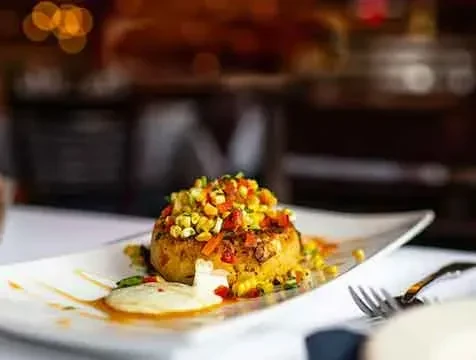 Gourmet round dish with corn, peppers, and sauces on a white plate.