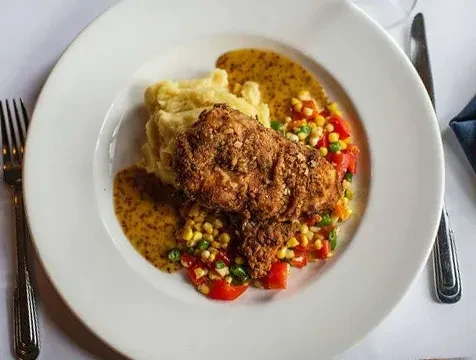 Plated crispy chicken, mashed potatoes, vegetables, and sauce with cutlery.