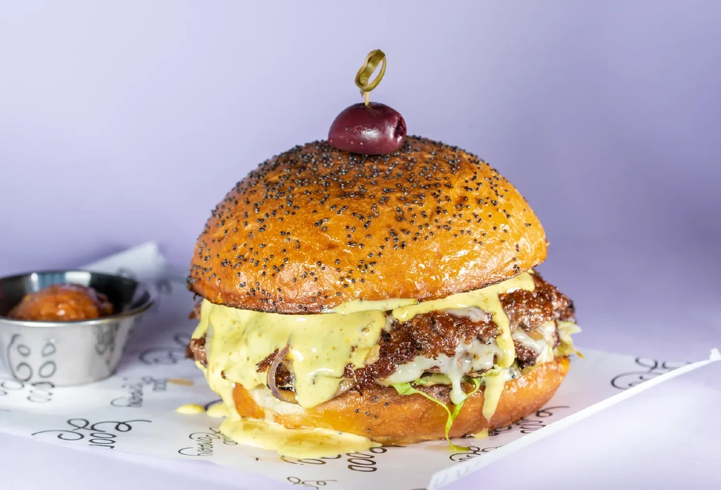 A gourmet double smash-burger with dripping cheese, onions, and an olive pick.