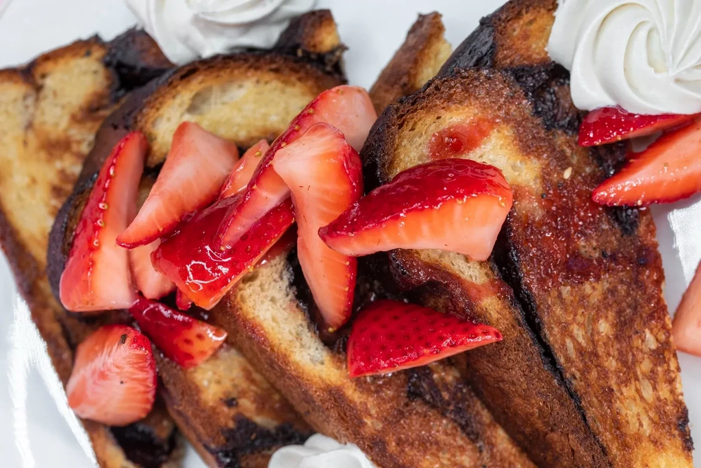 Golden French toast topped with sliced strawberries and whipped cream.