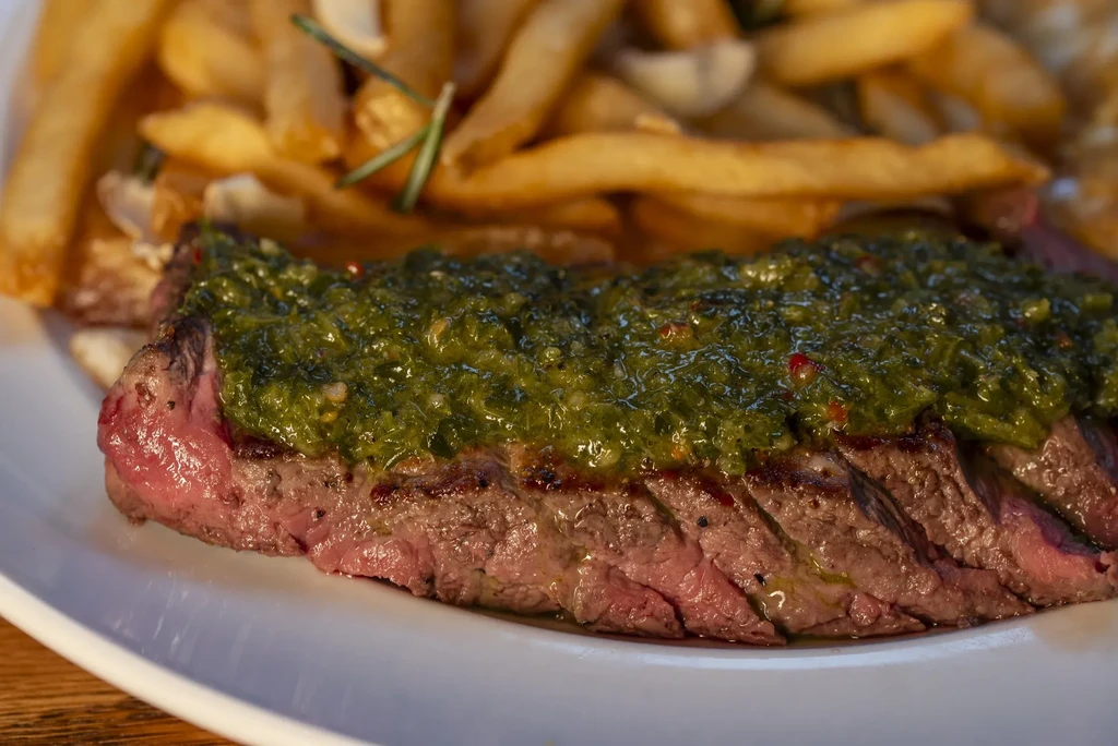 Sliced medium-rare steak with green sauce and rosemary french fries.