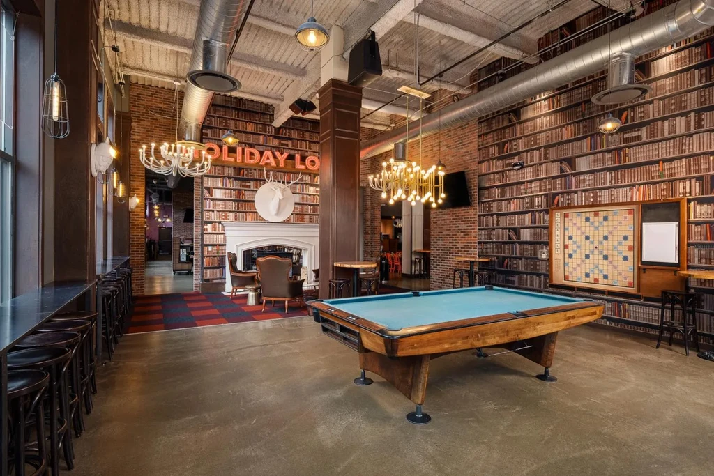 Stylish lounge with pool table, fireplace, 'HOLIDAY LOUNGE' sign, and mixed decor.