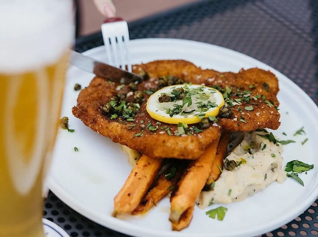 Close-up of schnitzel, carrots, and puree with a beer, being cut.