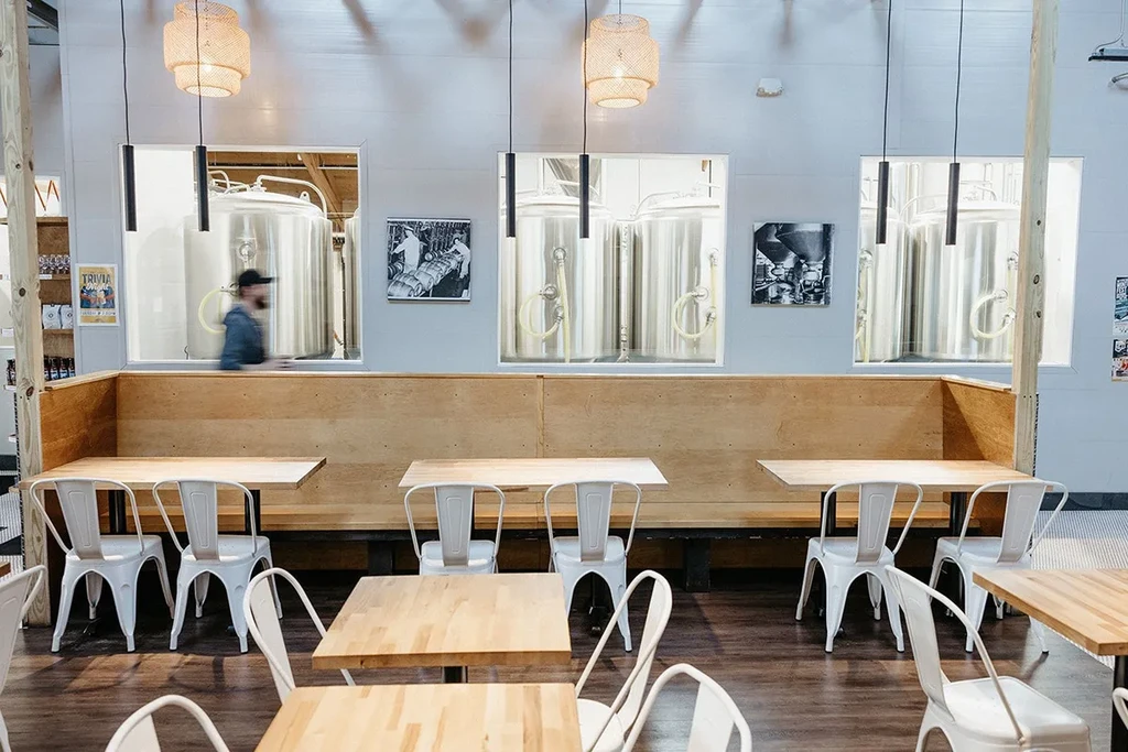 Bright brewpub dining room overlooks steel brewing tanks through wall cutouts.