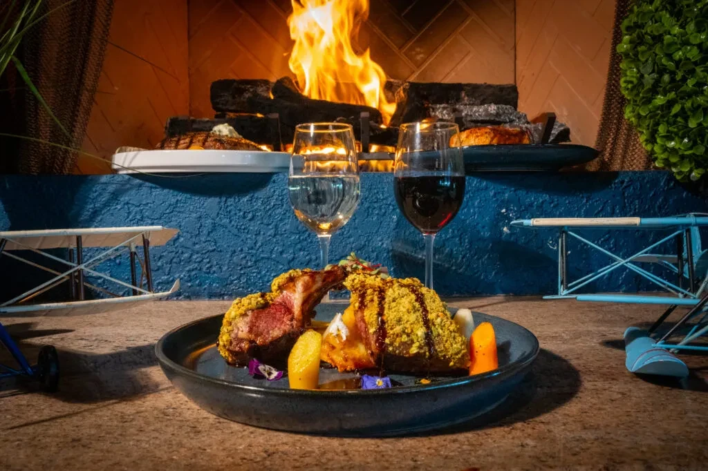 Plated meat, yellow topping, veggies, wine, fireplace, and aircraft models.