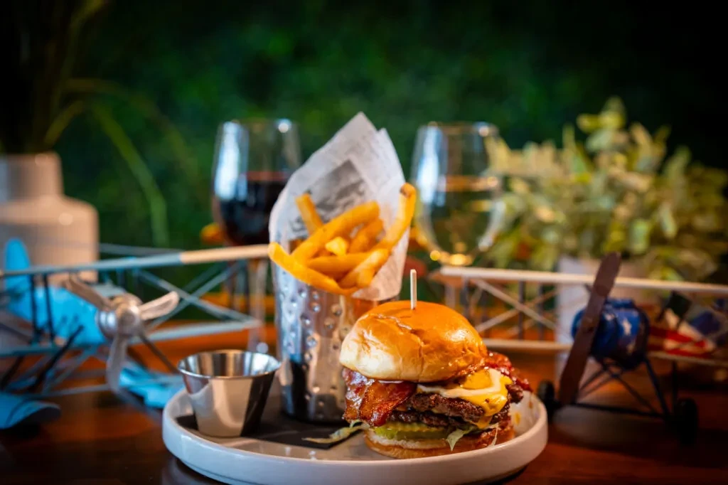 Gourmet burger with egg, bacon, cheese, fries, and biplane decor.