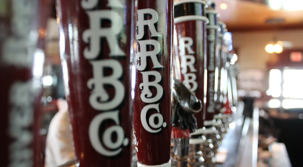 Dark red RRBCo. beer tap handle in focus at a bar.