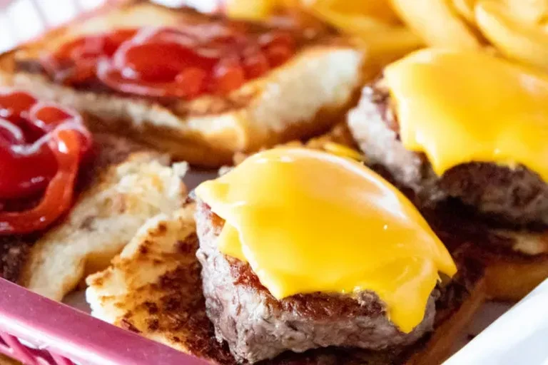 Mini cheeseburgers with cheese, ketchup, and fries in a red basket.