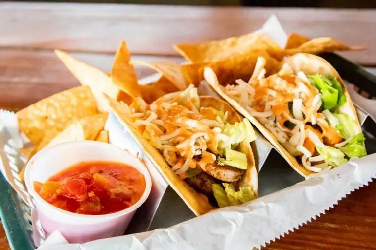 Close-up of two meat tacos, chips, and salsa in a green basket.