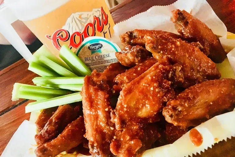 Basket of buffalo wings, celery, blue cheese, and a Coors beverage.