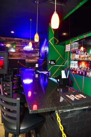 Modern bar with long granite counter, blue lighting, and glowing liquor bottles.