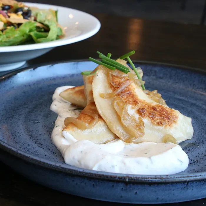 Golden-brown pierogi with caramelized onions, fresh chives, and creamy sauce.