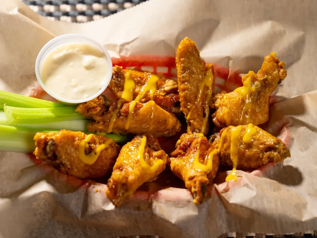 Basket of golden-brown chicken wings, yellow sauce, celery, and dip.
