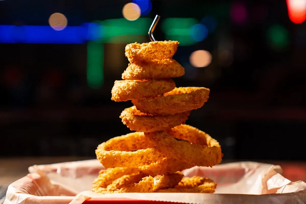 Golden-brown crispy onion rings stacked on a skewer in a red basket.