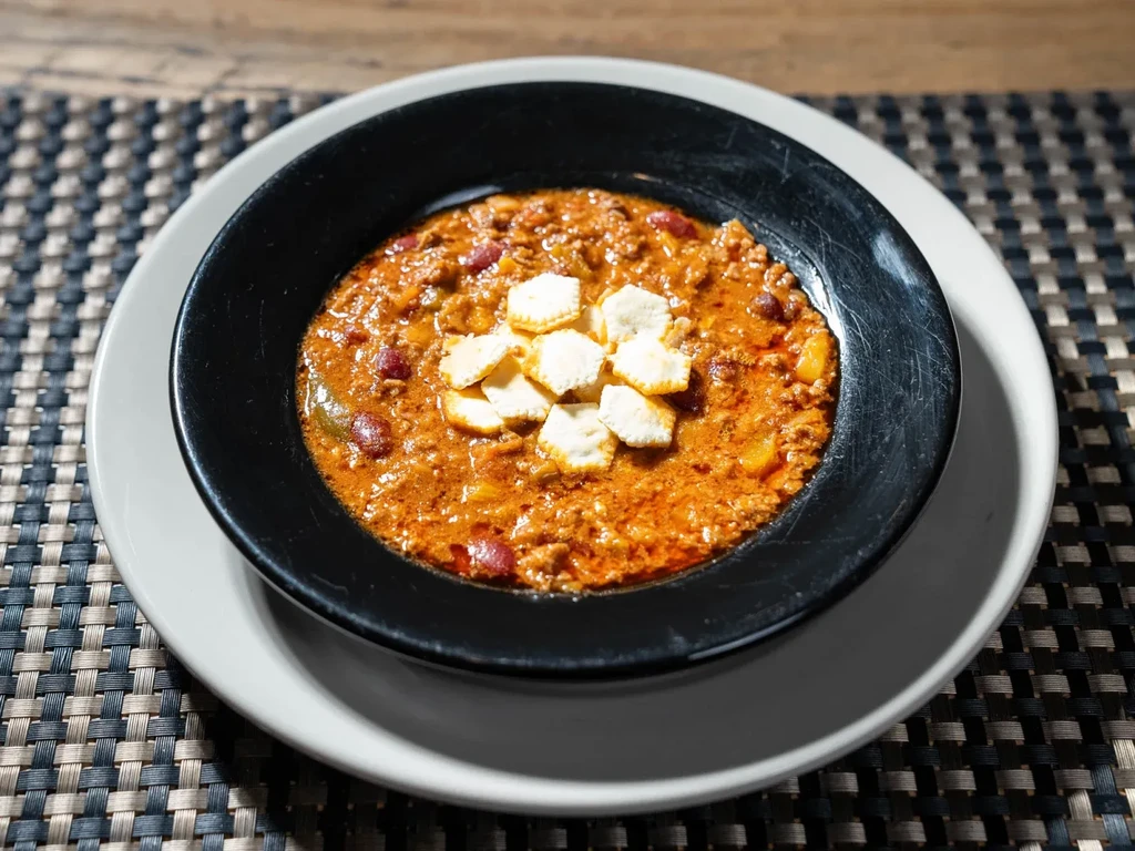 Close-up of a dark bowl of chili topped with square crackers.