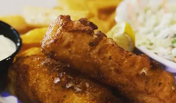Crispy battered fish and chips, with tartar sauce, coleslaw, and lemon.