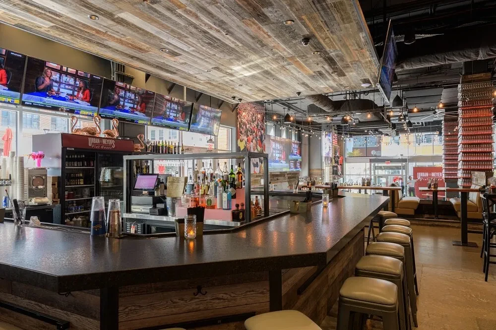 Modern sports bar interior with angular bar, stools, and TVs showing sports.