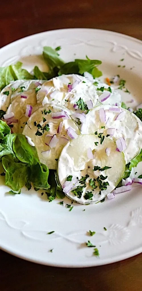 Top-down cucumber/zucchini salad with creamy dressing, red onion, and green herbs.