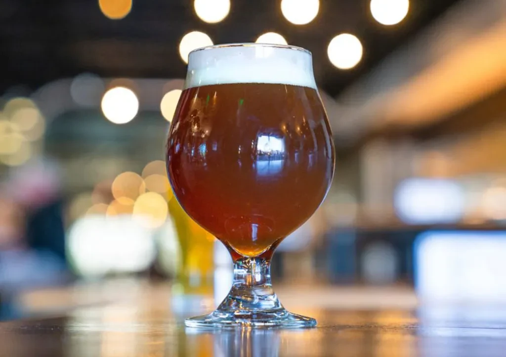Dark beer in a stemmed snifter with foam on a wood table.