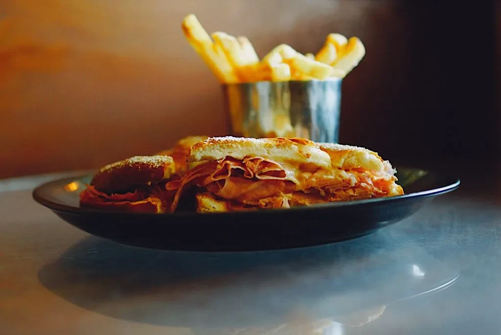 Golden-brown ham and cheese sliders served with fries on a dark plate.