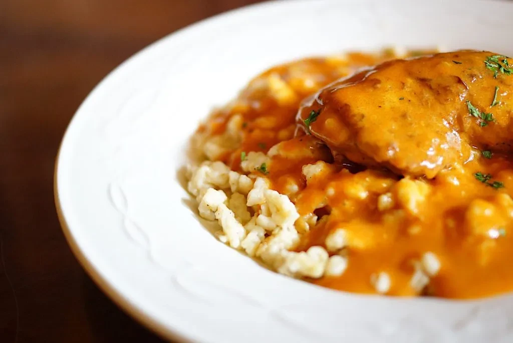 Chicken and spaetzle in creamy orange sauce, garnished with green herbs.