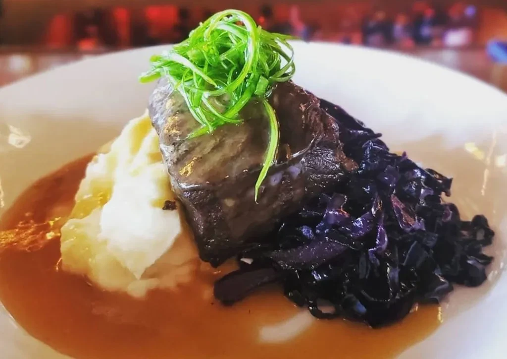 Braised meat, mashed potatoes, red cabbage, and gravy on a plate.