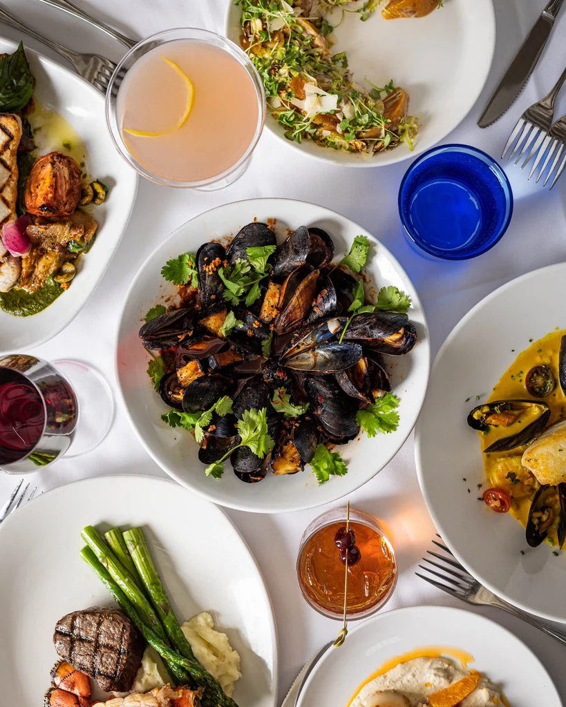 Mussels, steak, fish, scallops, wine, and cocktails on a dining table.