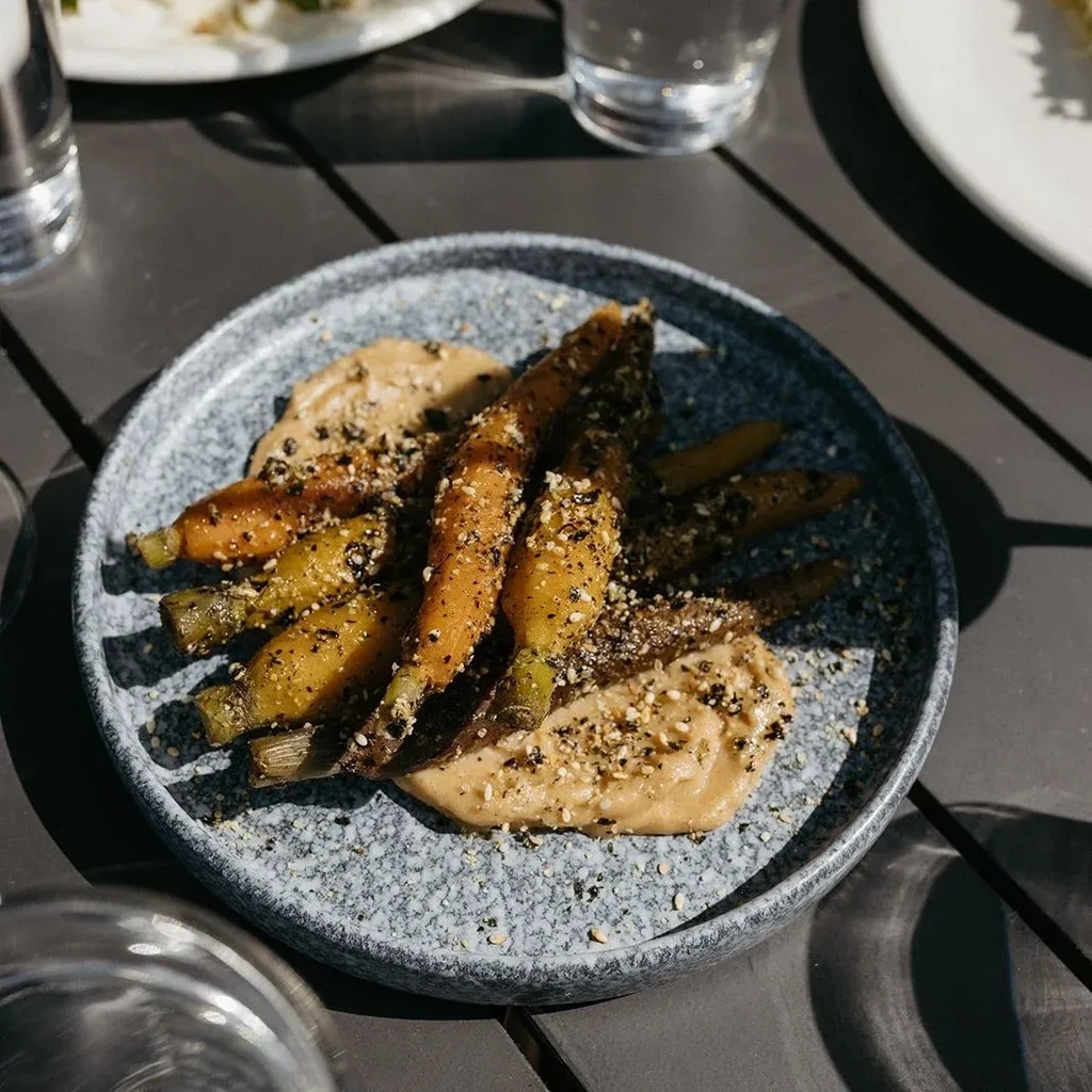 Roasted carrots on purée with sesame seeds on a grey plate.