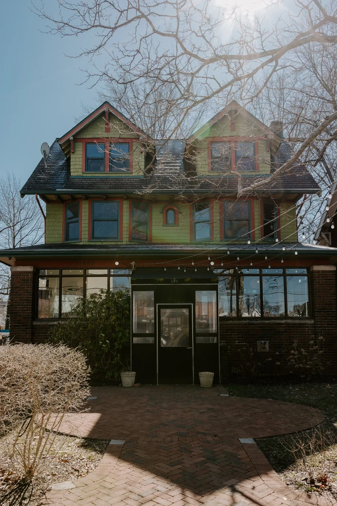 Two-story green building with red trim, brick path, and string lights.