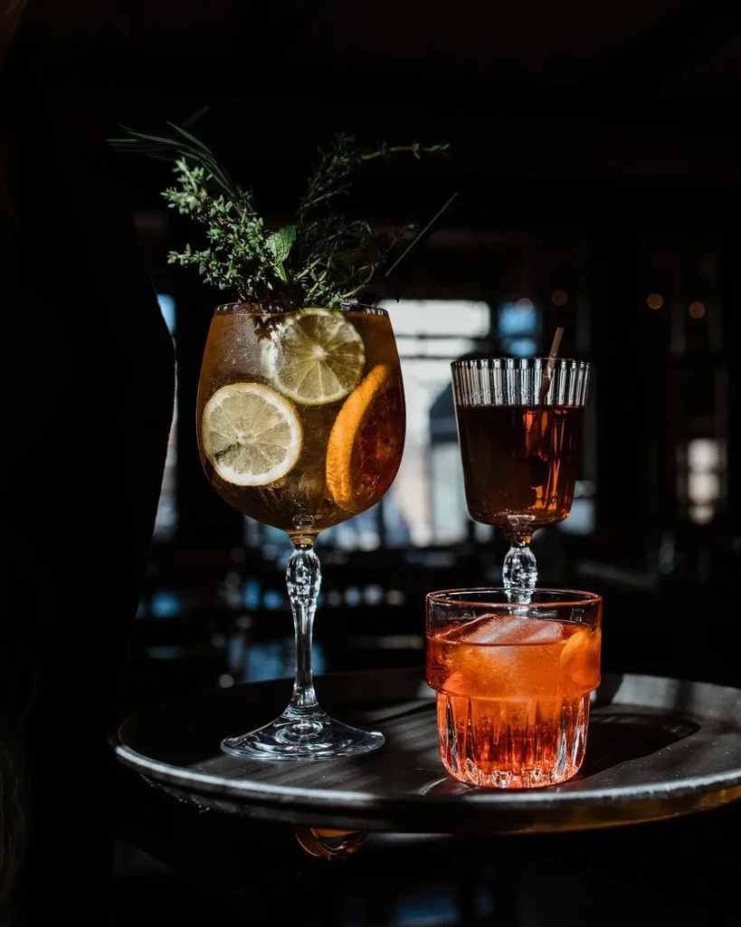 Three diverse cocktails, garnished with herbs and citrus, on a dark tray.